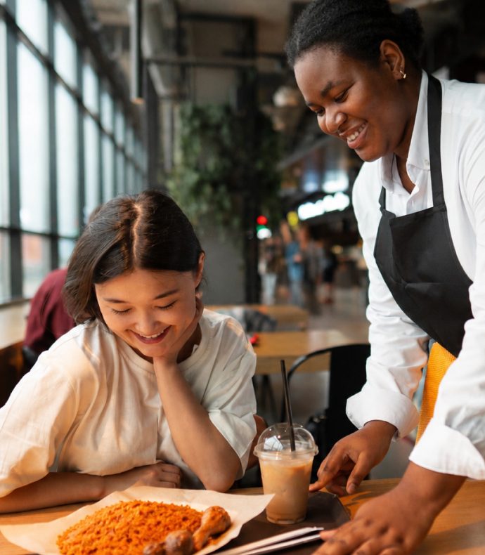 A server bringing jollof rice and a drink to a customer at Dee's
